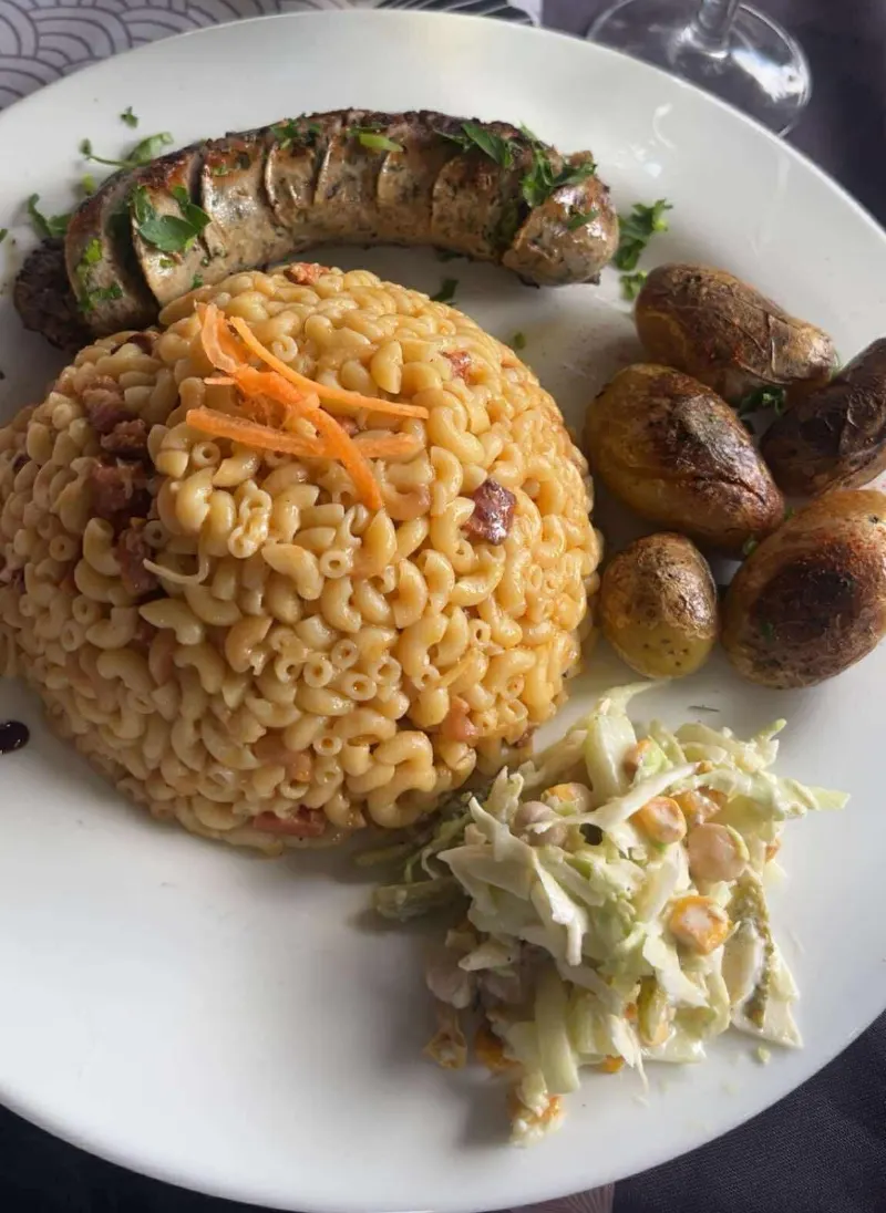 Une assiette du restaurant : saucisse grillée, macaronis gratinés, pommes de terre et salade de chou